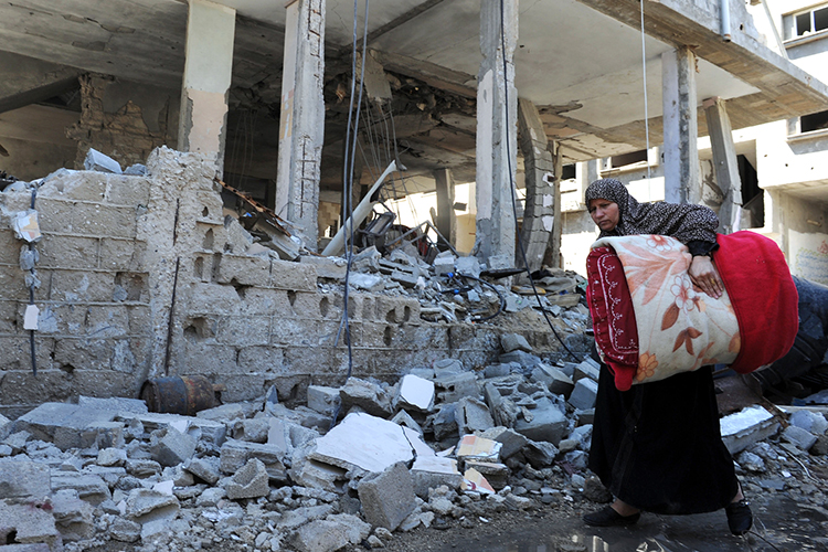 woman walking by a destroyed building in gaza