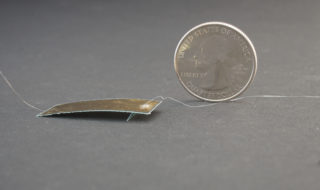 A photo of the small robot, which looks like a thin piece of metal, with a quarter for scale.
