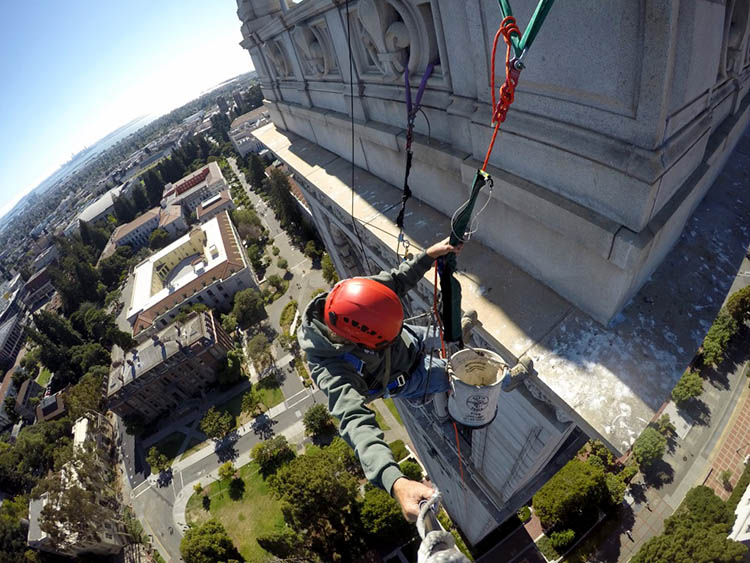 a man hangs off the side of the bell tower