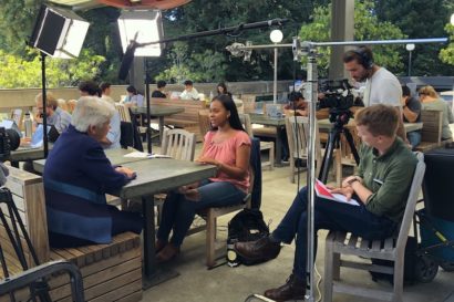 two people talk at a table surrounded by video equipment