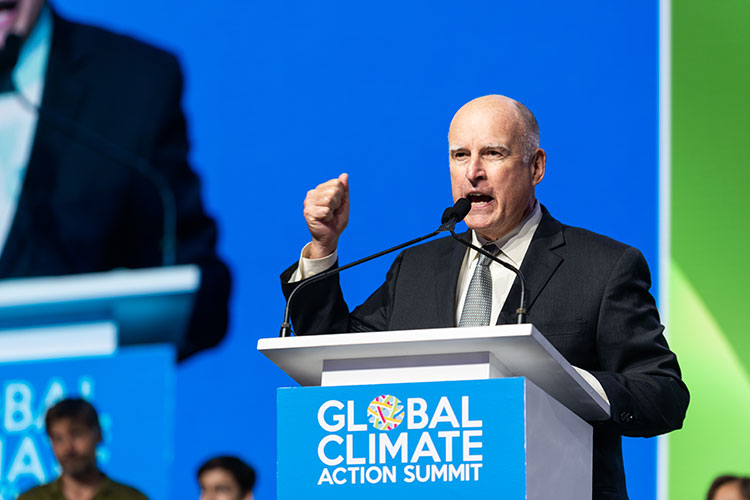 A photo of former governor Jerry Brown at a podium with his arm in the air
