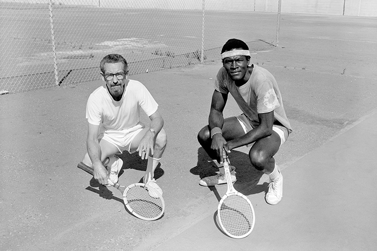 two men crouch with tennis rackets