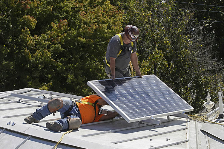 two men install solar panels on the roof of a home in California