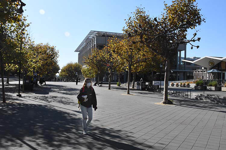 student in a n-95 mask walks through sproul plaza