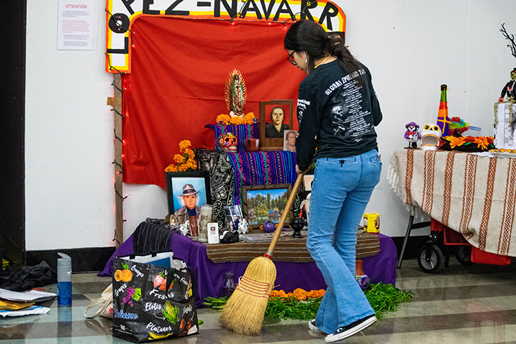 A student sweeps in front of her Day of the Dead altar