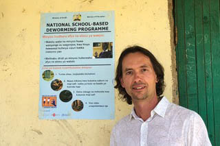 Miguel stands with a deworming poster in from of a stucco wall 
