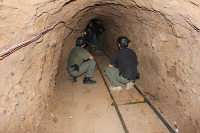 two men crouch in a smuggling tunnel