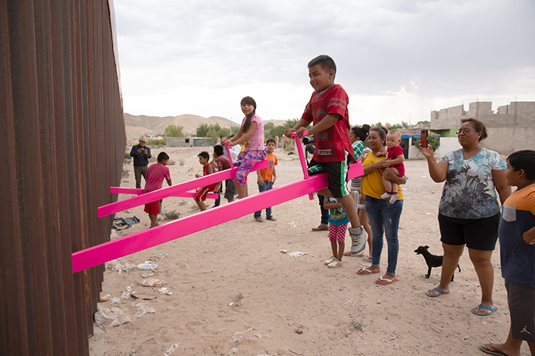 Young boy smiles as he rides a teeter totter on the border wall