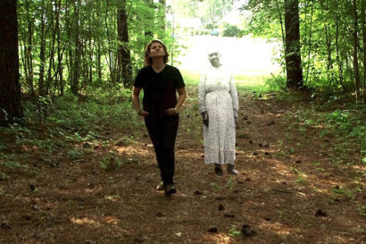 Frances Causey walks in the woods next to a representation of a slave