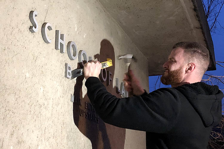 A man hammers off the B in Boalt Hall on the side of the Berkeley Law building