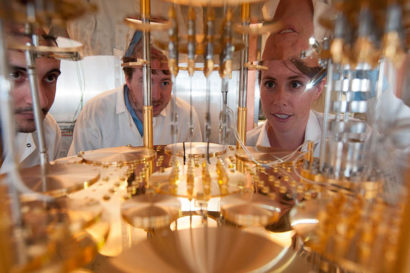 three people use a flashlight to peer into a scientific instrument