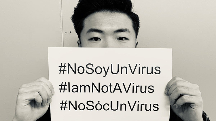 Man holds a sign up over his face that reads "I am not a virus."