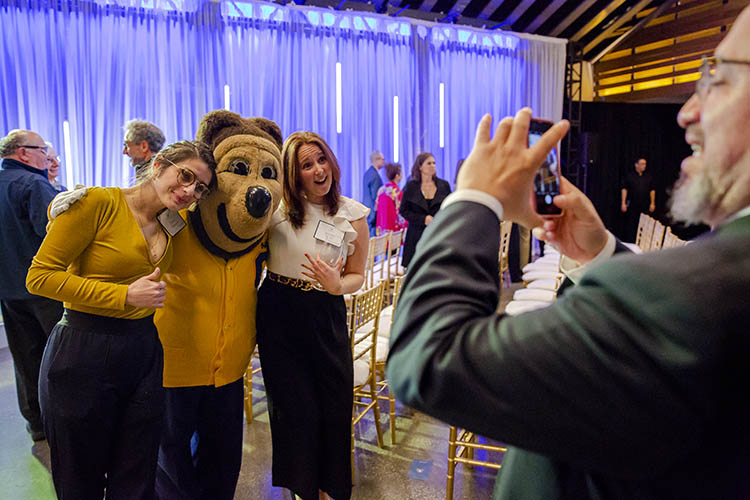 two women pose with oski while a man takes a picture