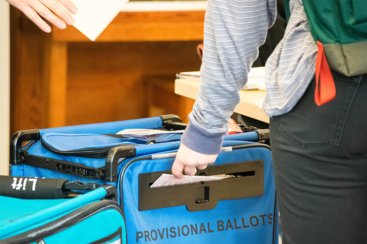 A person slipping a voting ballot into a box.