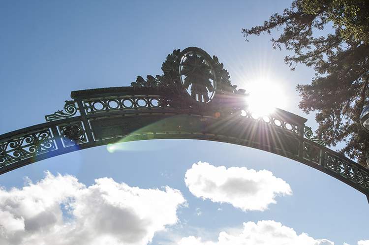 the sun shining through the fiat lux logo on sather gate