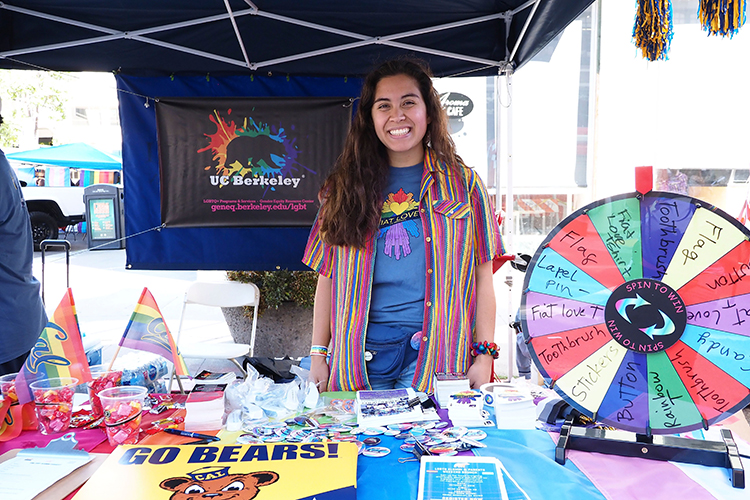 Micaela Camozzi standing smiling behind a table at a pride parade