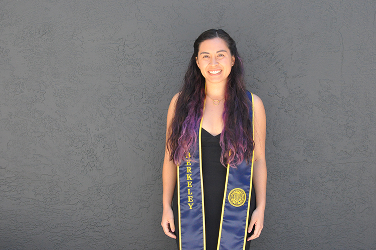 Micaela Camozzi posing in front of a black wall wearing graduation regalia