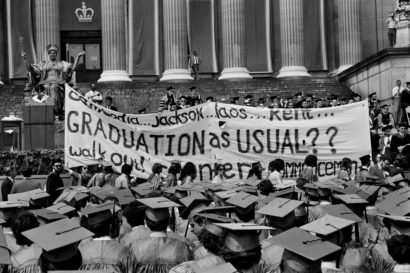 students hold a protest banner reading "graduation as usual?" during a commencement exercise