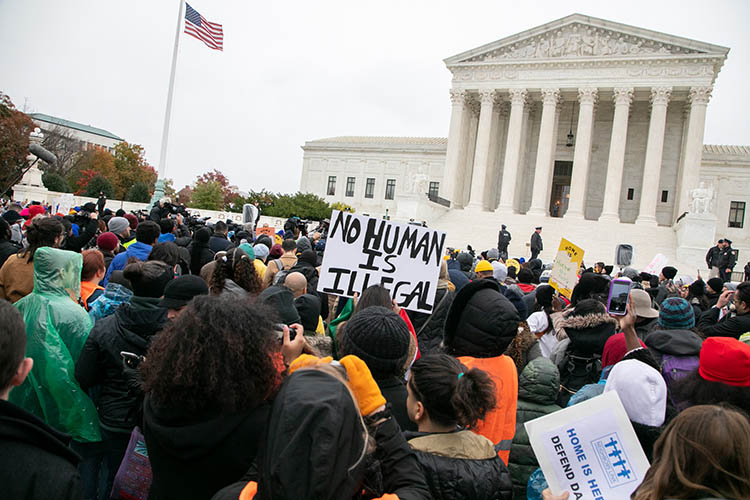 a crowd outside the supreme court building. One person holds a sign that says 