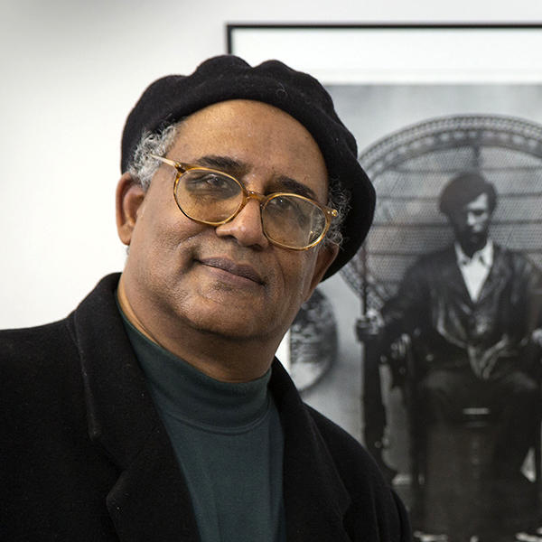 Waldo Martin wears a black beret posing in front of a photograph of Black Panther leader Huey P. Newton