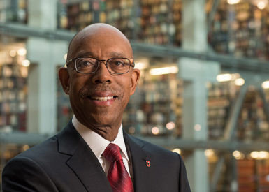 Michael Drake stands wearing a suit and tie, smiling