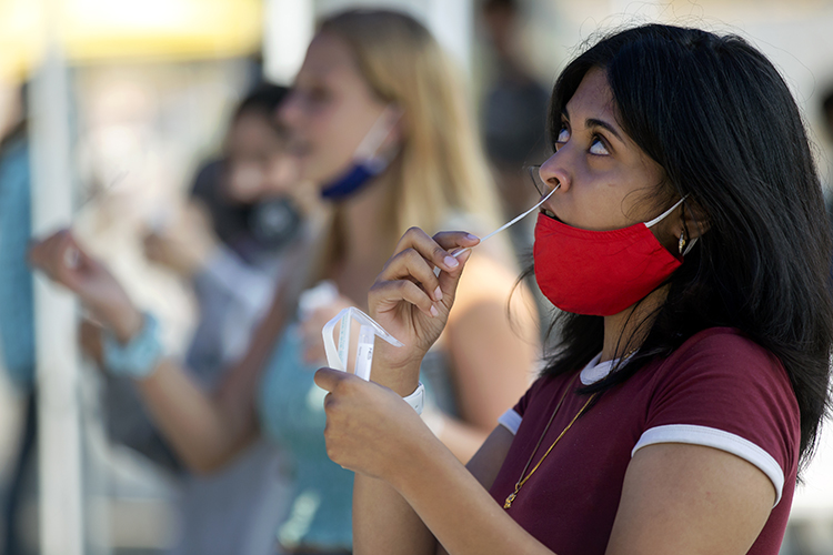 Supria Sharma, a first year student, sticks a swab up her nose doing a self-administered COVID-19 test at a University Health Services tent before school starts. SHe is wearing a red mask