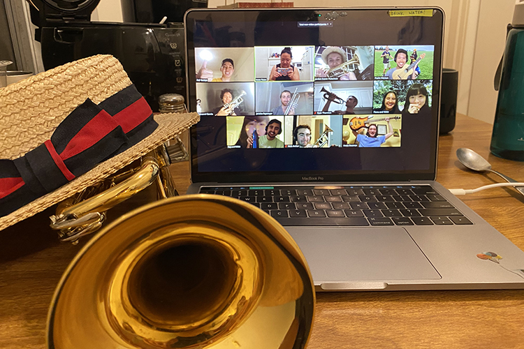 A photo of a computer screen where the Cal Band's trumpet players are having a bonding session. A straw hat and a trumpet are lying next to the computer screen.