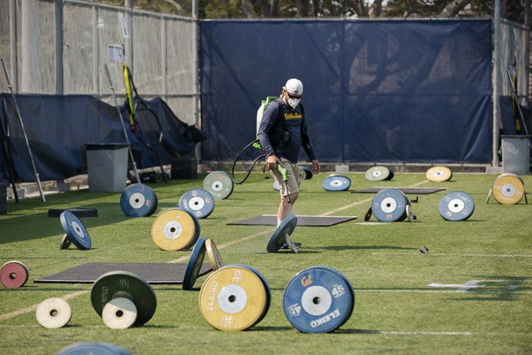 A Cal football staffer sprays weights with disinfectant on Maxwell Family Field