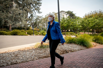 Wearing a face mask and a bright blue jacket, Chancellor Carol Christ walks toward her office in California Hall.