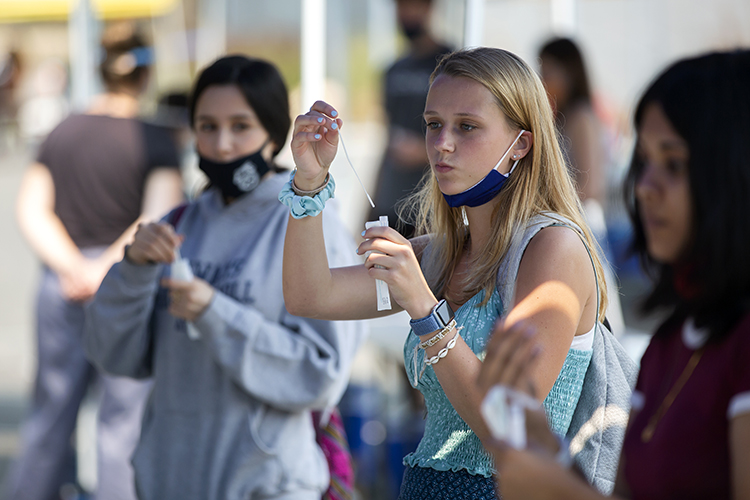 An incoming student named Paulina Calmes, from Russia, holds up a long-stemmed Q-tip swab and learns to do a nasal self-swab test for COVID-19 at a University Health Services tent before moving into her residence hall in fall 2020.