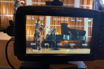 A violinist performs on stage next to a piano