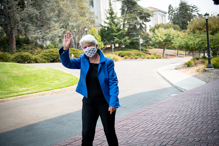 Chancellor Christ, wearing a blue jacket and a face mask, waves at the camera on her way into California Hall