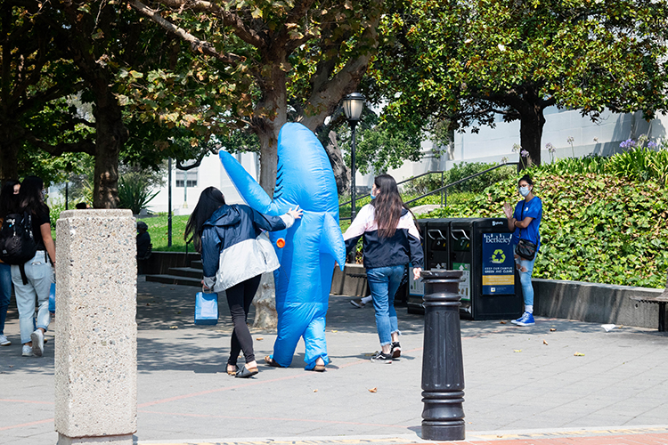 Three students, one in an inflatable blue shark costume, walk onto Sproul Plaza during the first week of remote instruction.