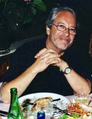 A photo of Geoffrey Nunberg sitting at a table with his hands clasped in front of him.