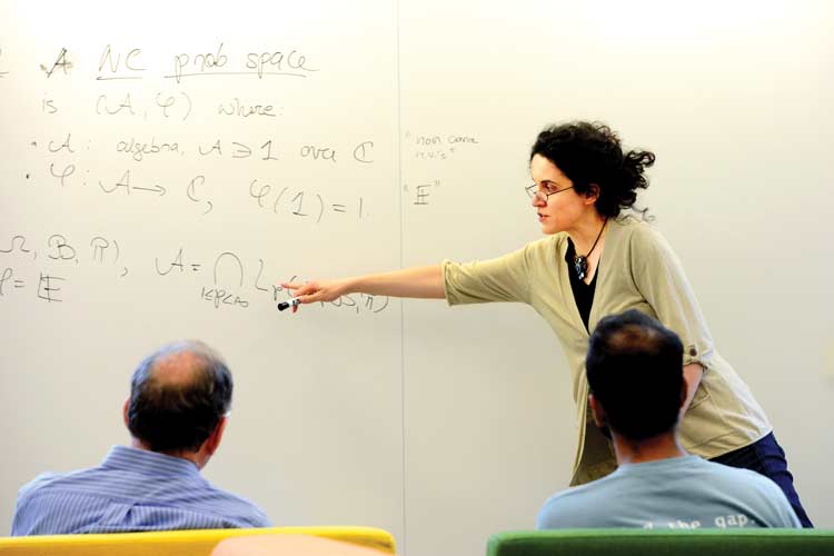 woman discussing math in front of whiteboard, two men looking on