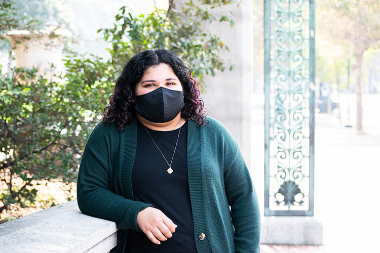 ASUC president Victoria Vera, wearing a black face mask, stands near Sather Gate.