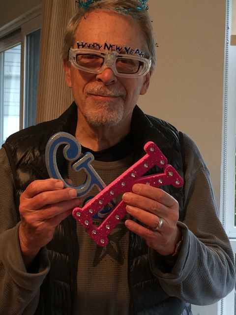 A photo of Geoffrey Nunberg wearing party glasses that say "Happy New Year" and holding plastic letters "G" and "K"