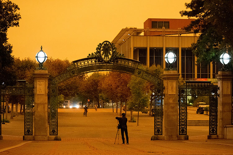 A student shoots a photo using a tripod set up on Sproul Plaza on a day when smoke and fog turned the sky orange.