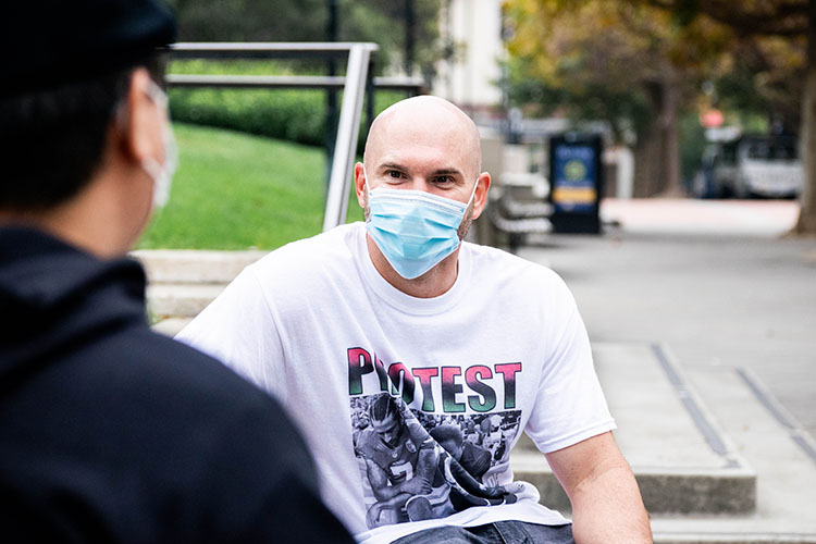 Kevin McCarthy talks with admissions officer Henry Tsai, wearing a face mask during the pandemic and a protest T-shirt with a photo of Colin Kaepernick and MLK Jr. both kneeling.