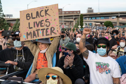 girl holds black lives matter sign in the middle of hundreds of protestors