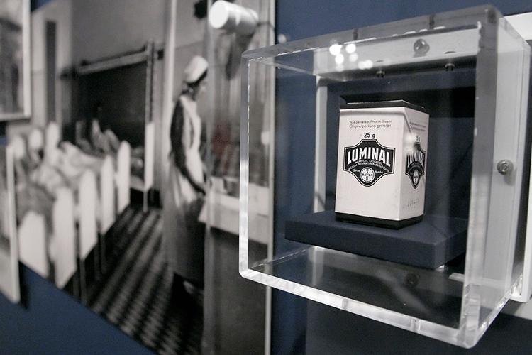 A photo of a tin container labeled "Luminal" behind a glass case as part of a museum exhibit