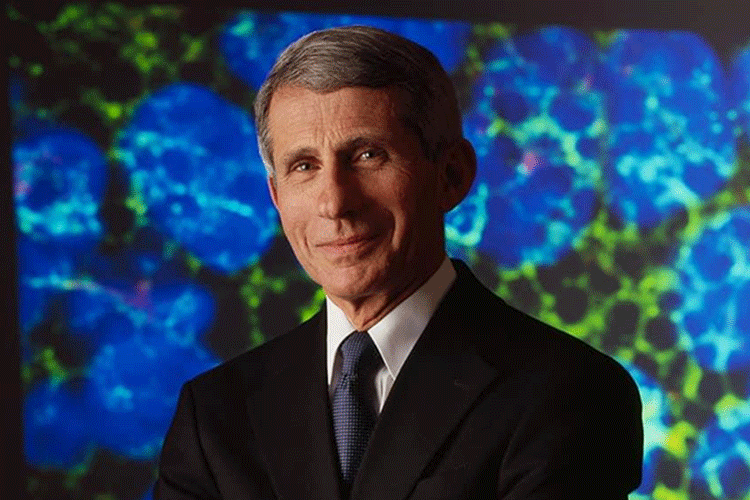 A portrait of Anthony Fauci wearing a black suit with a white tie, and standing in from of a cellular microscope image.