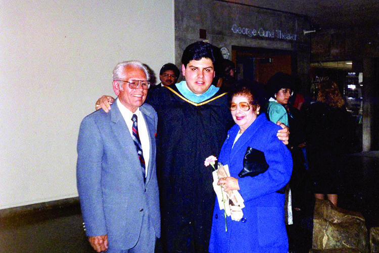 castro stands in a cap and gown with his arms around his grandparents