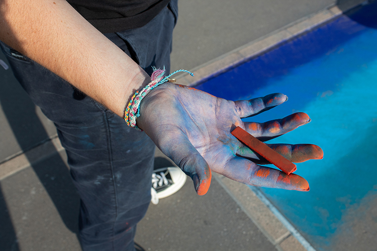 A chalk artist holds chalk in their hand which is stained with blue chalk