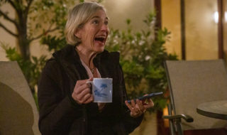Jennifer Doudna laughs with a cup of coffee in her hand and a phone in the other hand