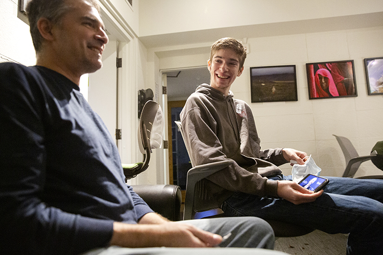 Jamie and Andy Cate sit together laughing while watching a press conference on a phone