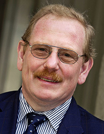 Reinhard Genzel smiles at the camera in a blue jacket and striped shirt