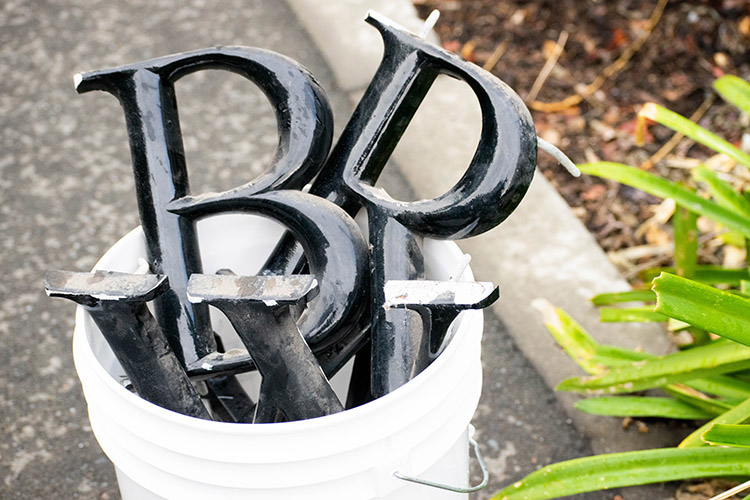 Black metal letters spelling Barrows Hall sit in a white bucket after work crews removed them from the building, which has now been unnamed.