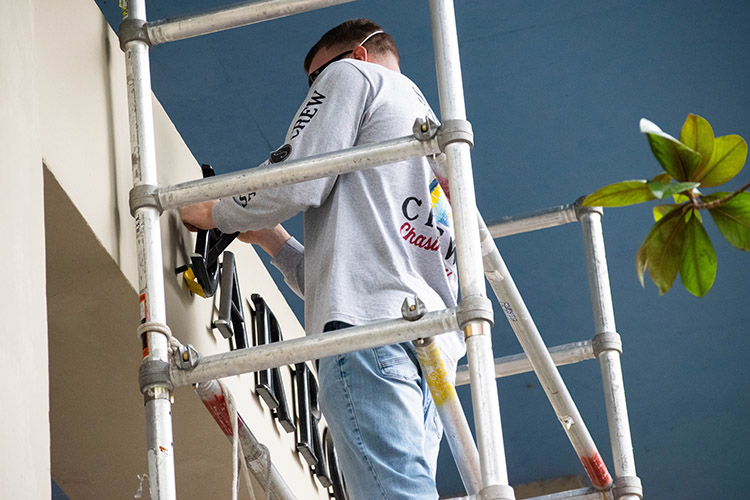 A worker on scaffolding removes metal letters spelling Barrows Hall.