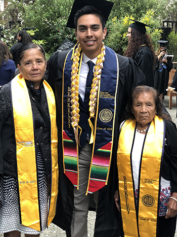 Bryan Osorio Trujillo's two grandmothers stand next to him in a photo from his 2018 Latinx Graduation ceremony. All of them are wearing graduation stoles.